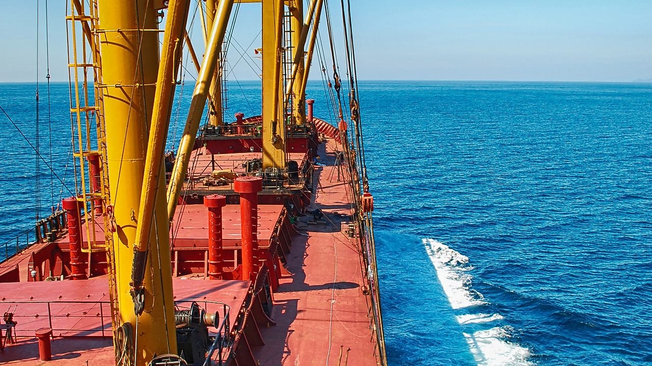 Deck of a large cargo vessel with yellow cranes sailing in open sea.