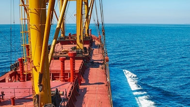 Deck of a large cargo vessel with yellow cranes sailing in open sea.