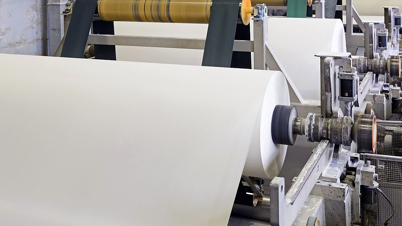 Paper rolls being processed on an industrial paper manufacturing machine.