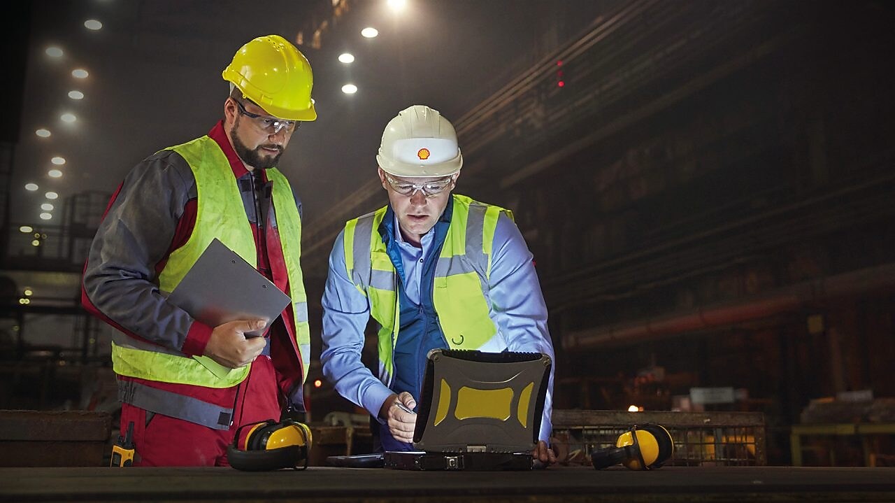 Steelworkers using laptop in dark steel mill