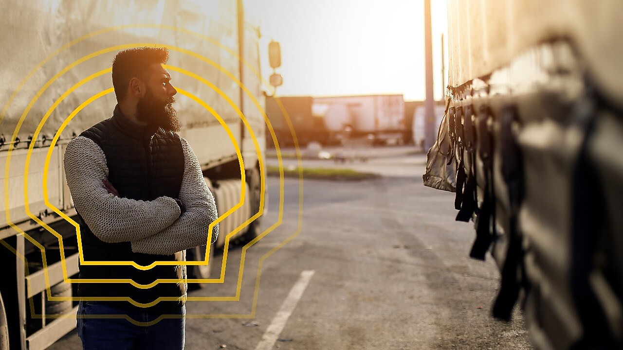 A man looking at a truck with his arms crossed. The Shell pecten outline is around him.