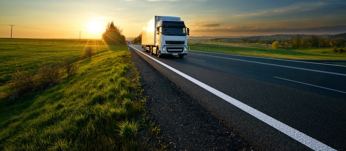 White truck driving along a country road at sunset.