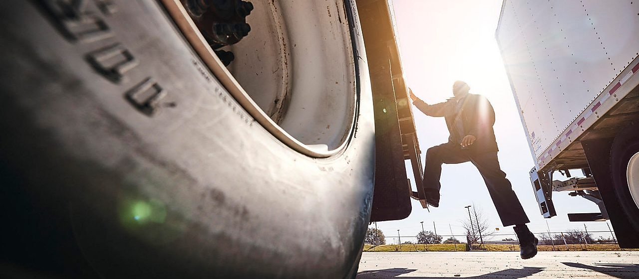 A close up of a truck wheel with the driver stepping down from the truck in the distance