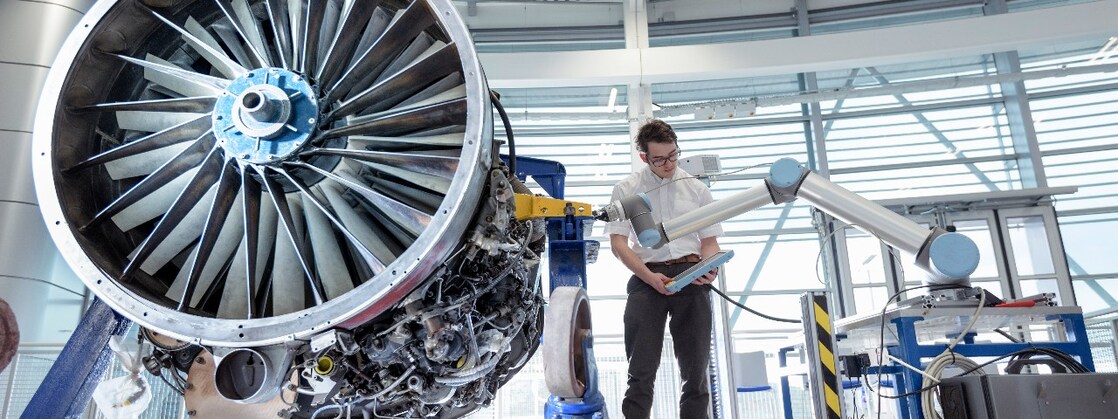 Engineer using robotic arm to service jet engine in robotics research facility