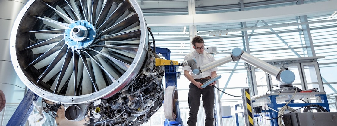 Engineer using robotic arm to service jet engine in robotics research facility