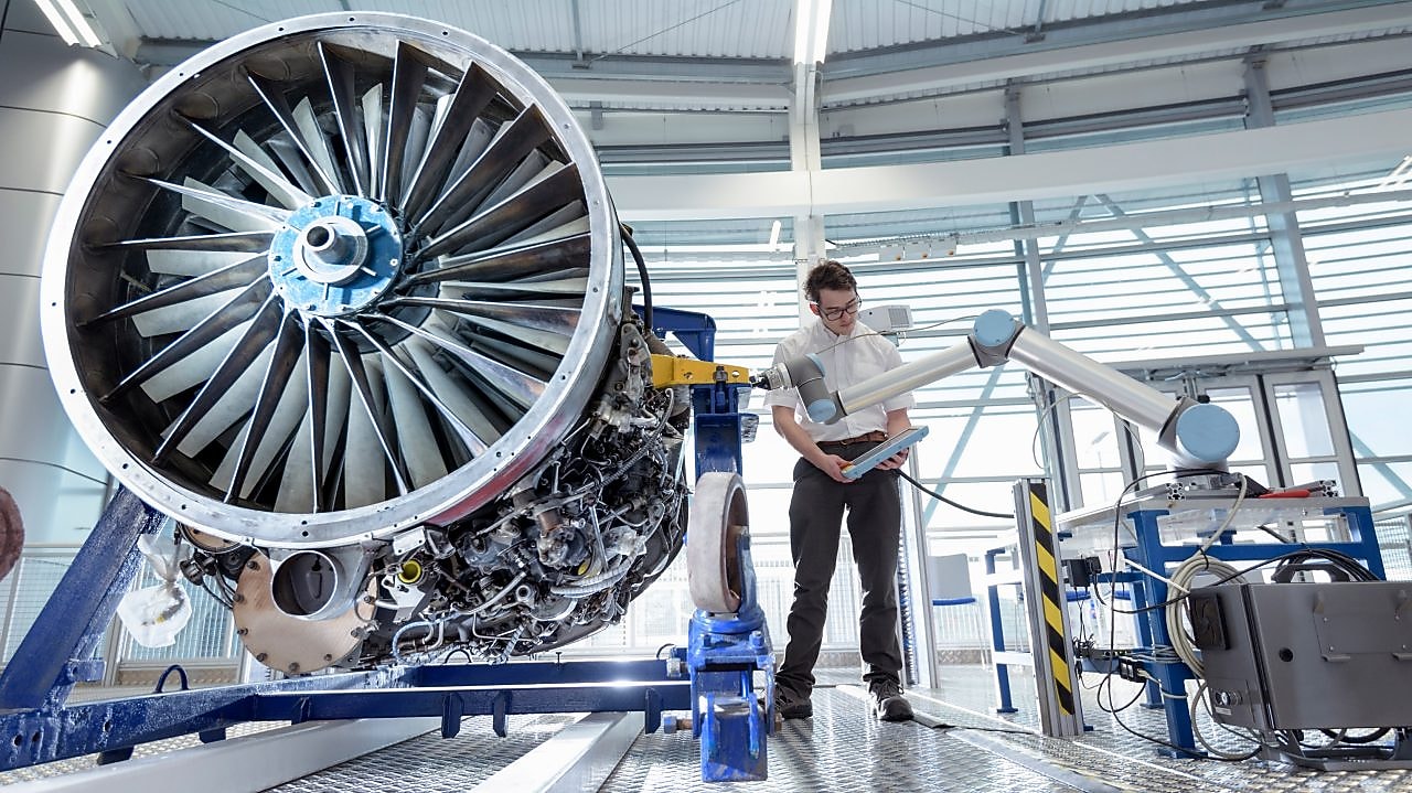 Engineer using robotic arm to service jet engine in robotics research facility