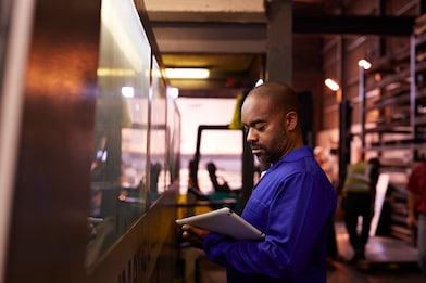 Steel worker looking at tablet standing next to big laser cutting machine