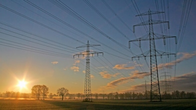 High voltage electrical power lines against the sunrise in the background.