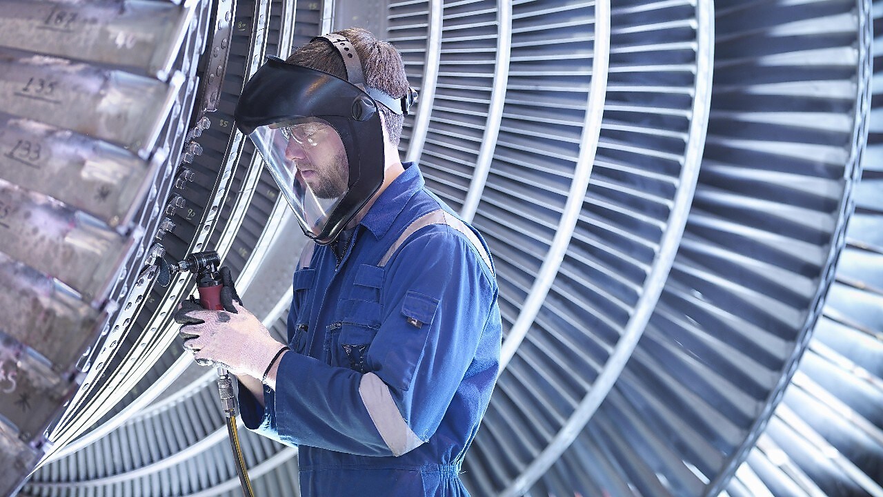 Engineer repairing steam turbine blade with grinder in workshop