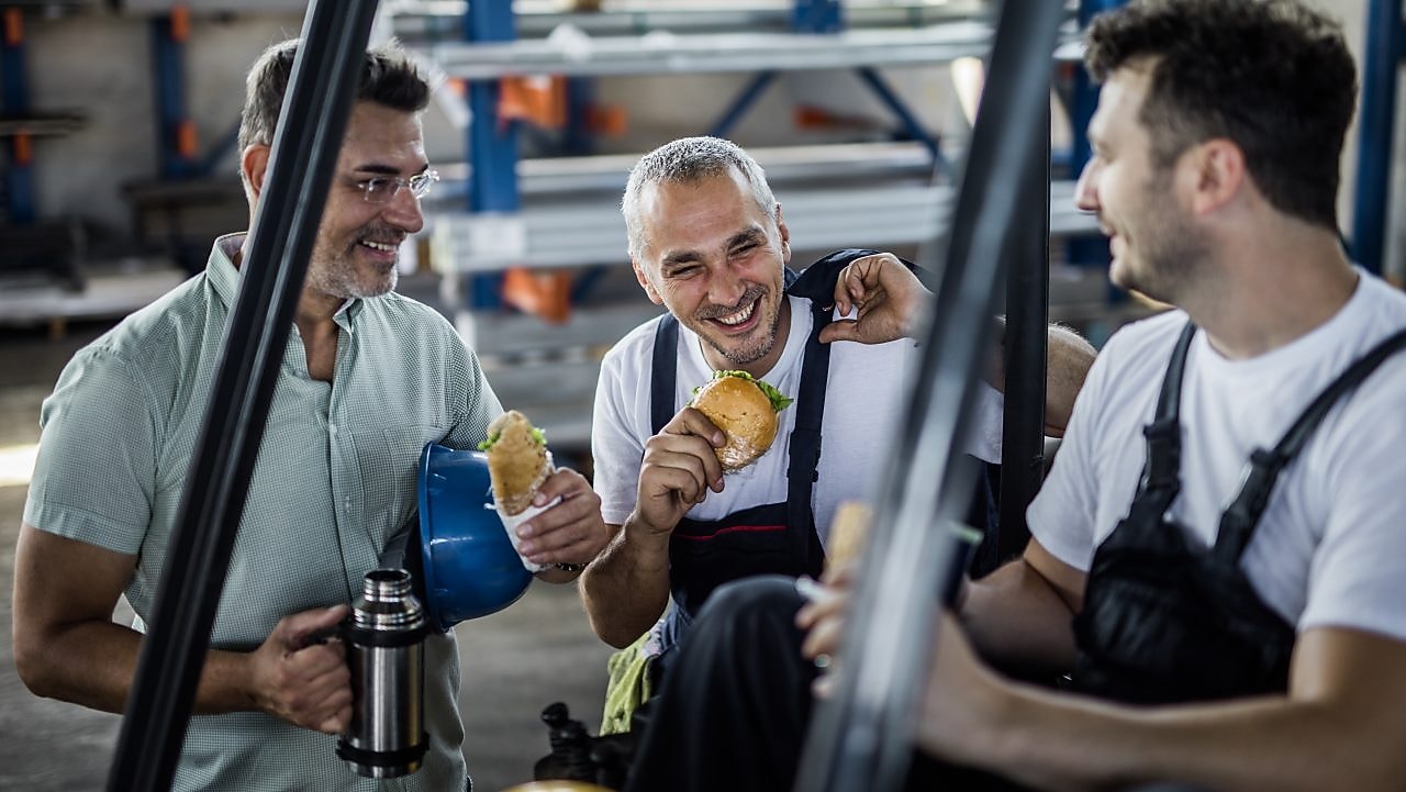 happy manual workers and their manager talking on a lunch break in a factory