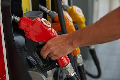 Close-up of a hand holding a red Shell fuel pump nozzle at a multi-grade fuel dispenser.