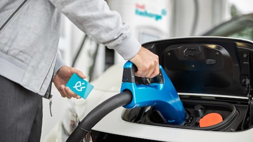 Close-up of a hand inserting a blue charging connector into an electric vehicle's charging port while holding a contactless charging card.