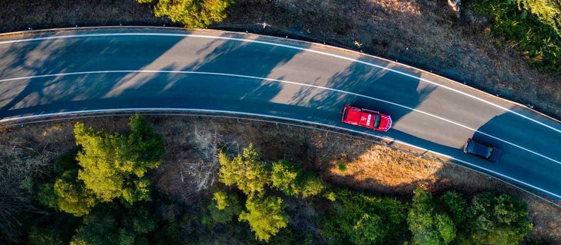 Red and black cars driving on a road with green trees on the side