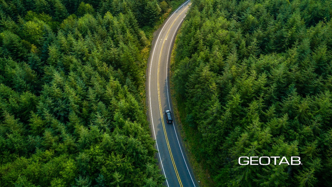 Aerial view of a car driving through a forest. Geotab logo present on bottom right corner of the image.