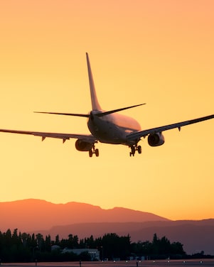 Silhouette of an airplane flying above clouds with a vibrant sunset sky in the background.