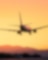 Silhouette of an airplane flying above clouds with a vibrant sunset sky in the background.