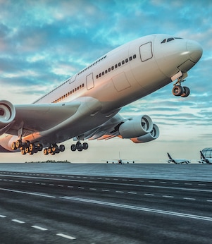 A large commercial airplane taking off from a runway at sunset, with landing gear still extended and the sky filled with colorful clouds.