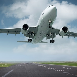 Airplane taking off from a runway, captured from below with landing gear still extended against a blue sky with clouds.
