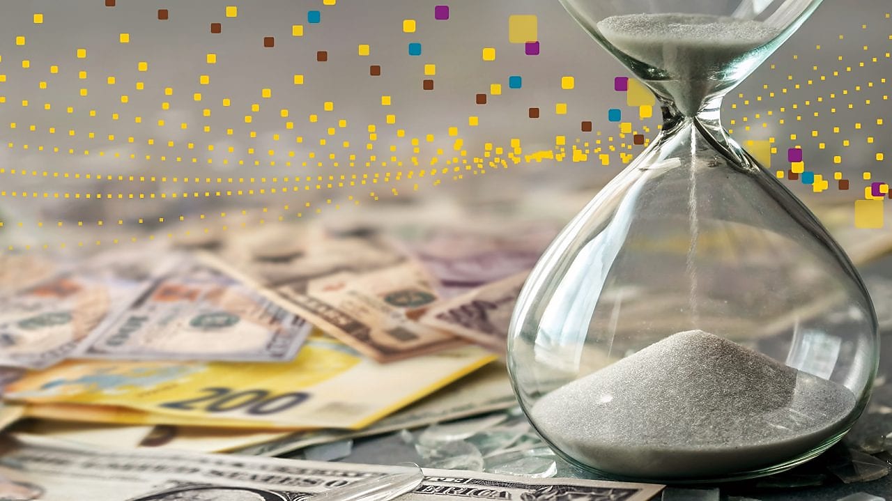An hourglass filled with sand sits beside a scattered pile of international banknotes, with abstract digital dots in the background, symbolising time pressure and financial or economic uncertainty.