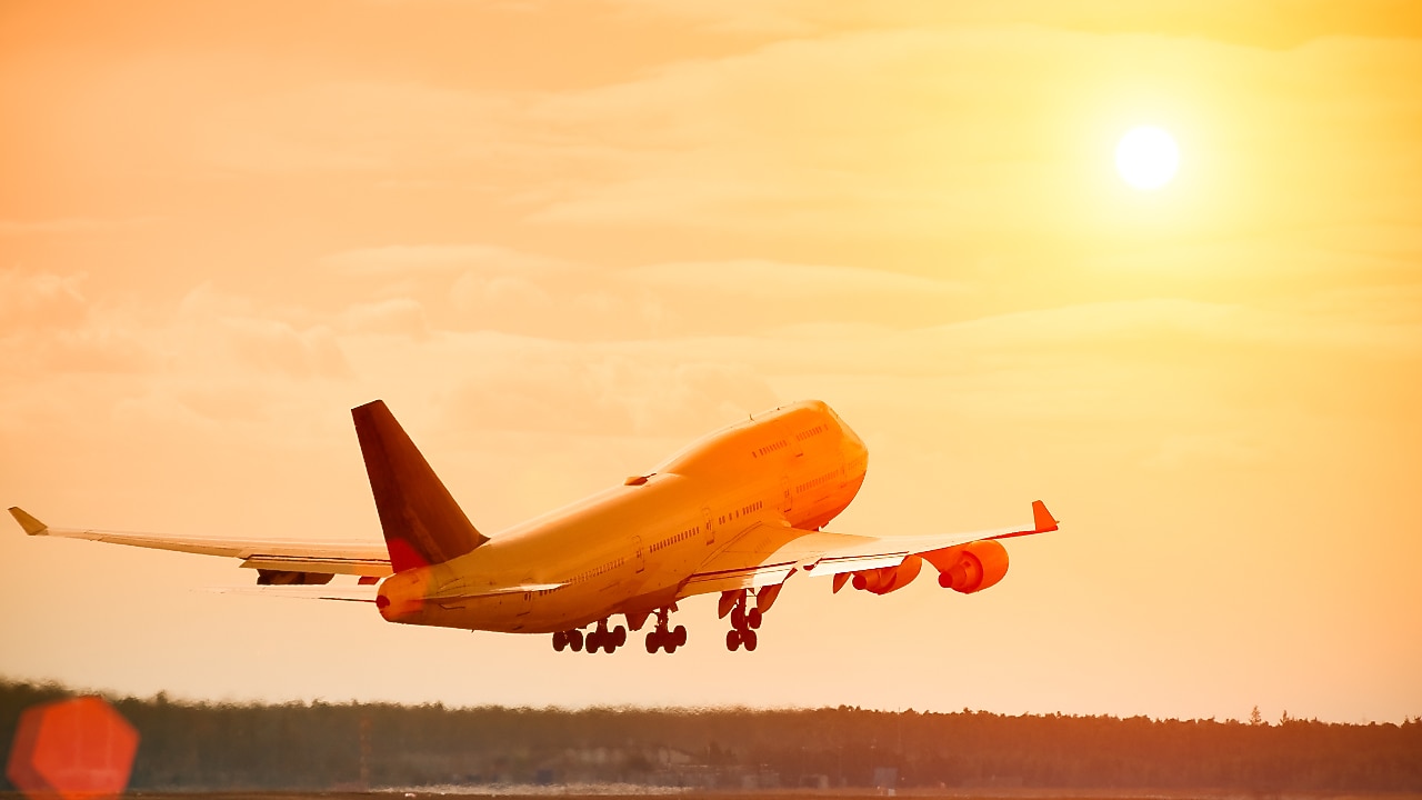 Commercial aeroplane lifting off the runway at sunset, with an orange glow reflecting off the fuselage and sky.