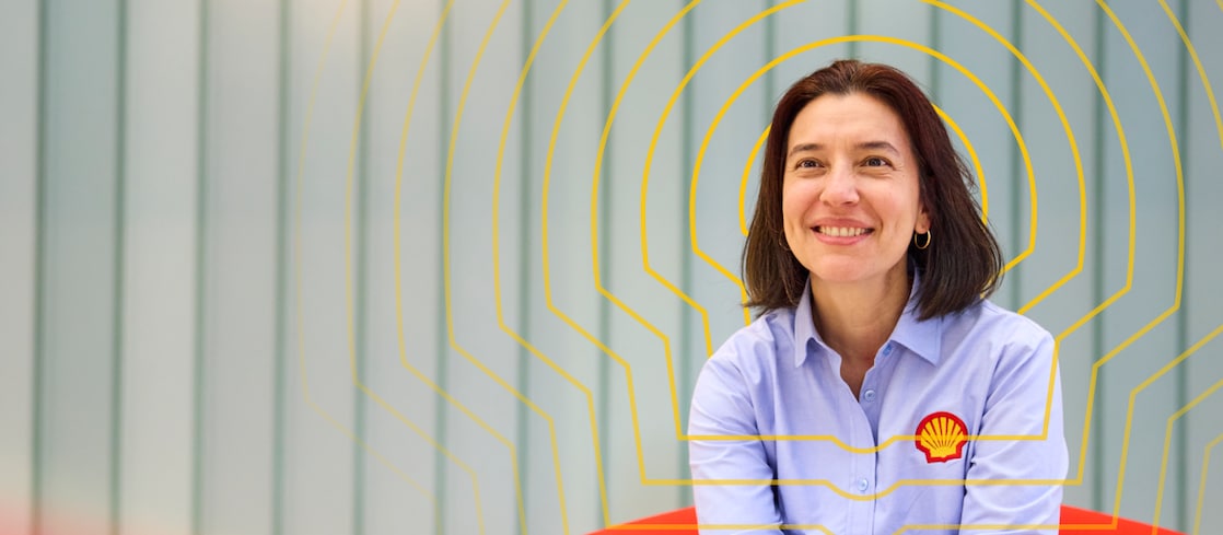 A smiling woman in a light blue shirt seated against a grey background with yellow Shell line graphics around her.