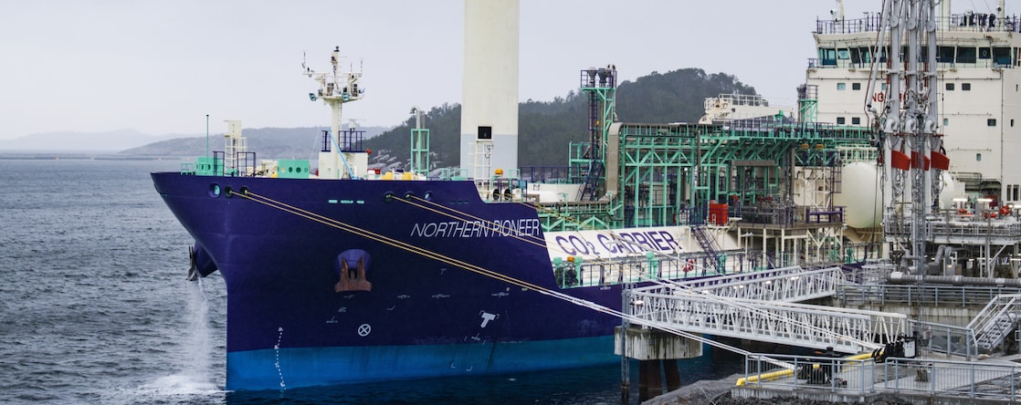 Aerial view of a large Shell vessel on blue water near a coastal industrial site.