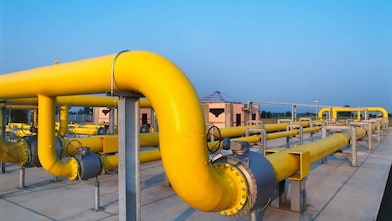 Large yellow industrial gas pipelines at a processing facility under a clear blue sky.
