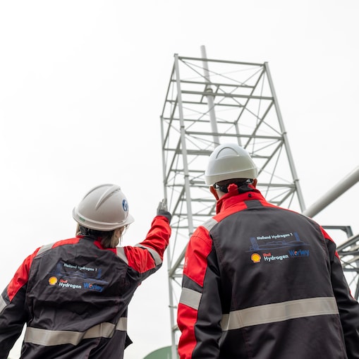 Two workers in hard hats and safety clothing looking up at industrial infrastructure.