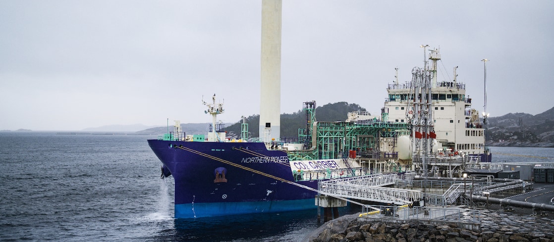 Aerial view of a large Shell vessel on blue water near a coastal industrial site.