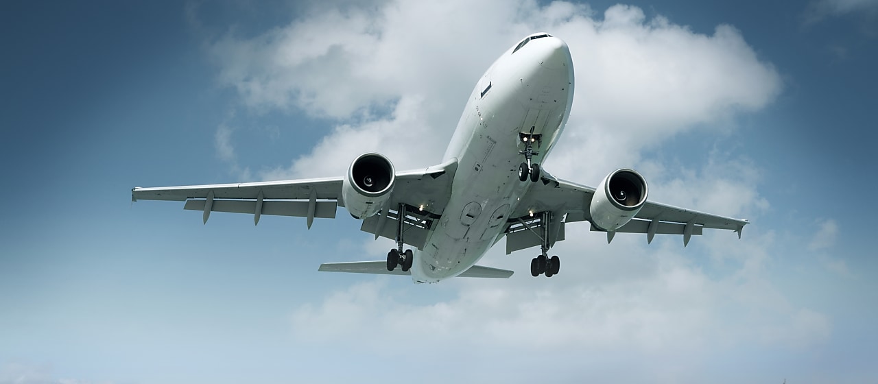 A large commercial airplane taking off from a runway with its landing gear still extended, under a partly cloudy blue sky.