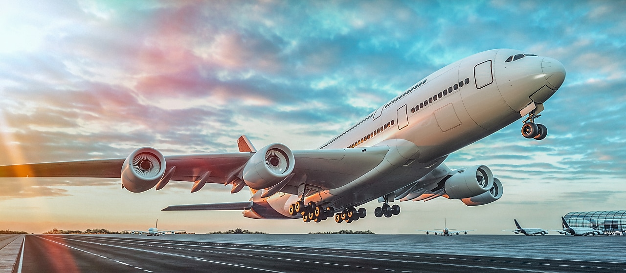 A large commercial airplane taking off from a runway at sunset, with landing gear still extended and the sky filled with colorful clouds.
