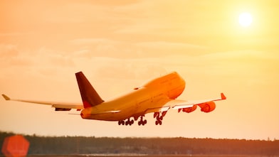 Commercial aeroplane lifting off the runway at sunset, with an orange glow reflecting off the fuselage and sky.