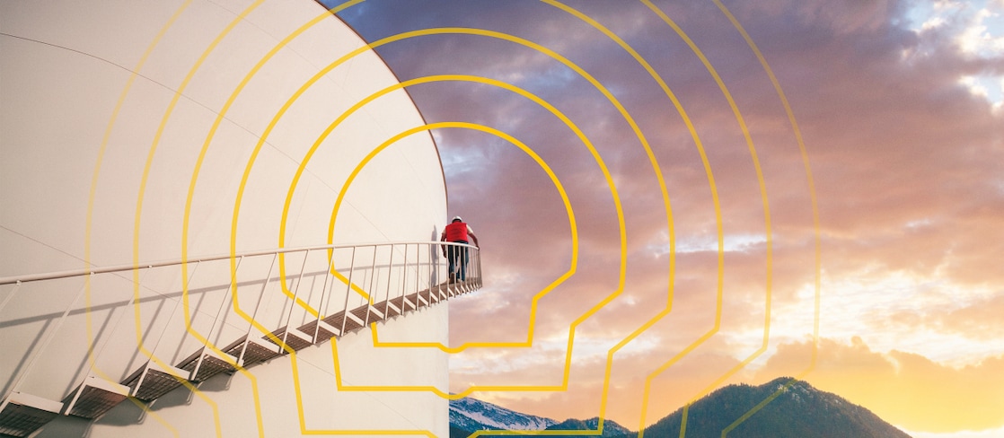 Person standing on stairs attached to a large white industrial tank, with a mountainous lake landscape and a yellow Shell logo overlay in the foreground.