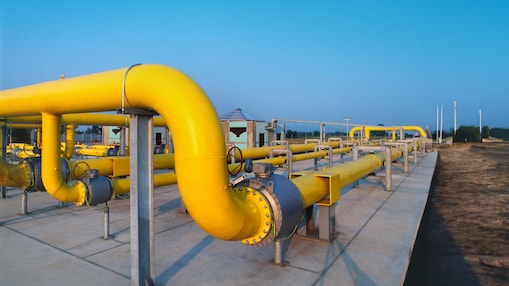 Large yellow industrial pipelines at a gas processing or distribution facility, with valves and metal supports under a clear blue sky.