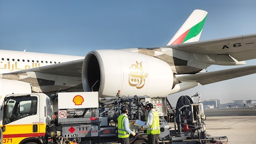 Shell Aviation fuel truck refuelling an Emirates aircraft on the tarmac, with two technicians in high-visibility jackets operating the equipment.