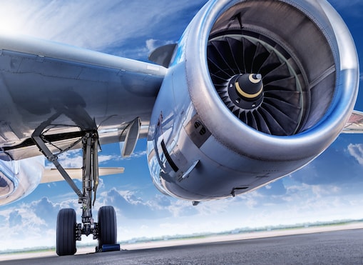 Close-up view from beneath a commercial airplane showing the aircraft's landing gear and jet engine against a bright blue sky.