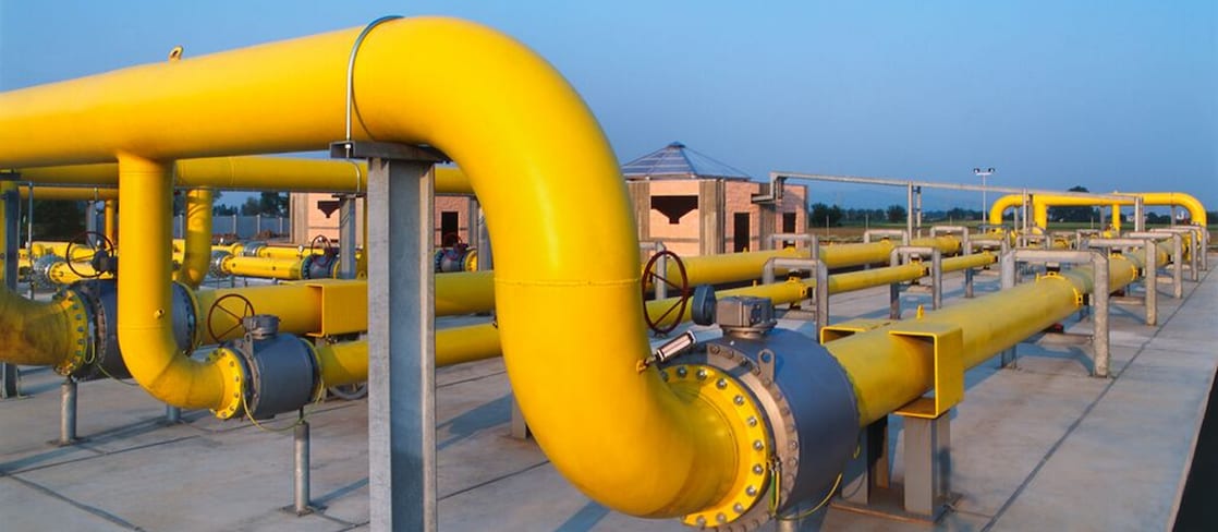 Large yellow industrial gas pipelines at a processing facility under a clear blue sky.