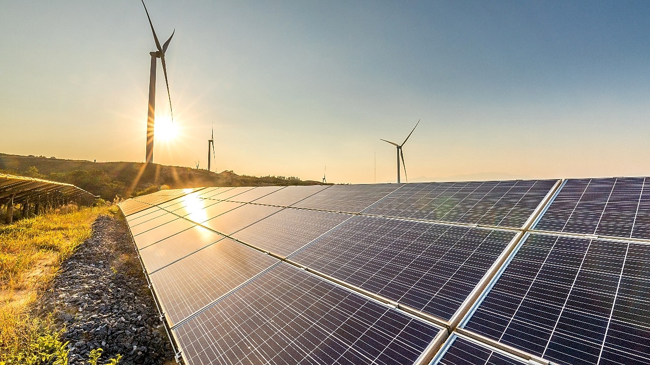 Solar panels and wind turbines generating renewable energy in a field at sunset.