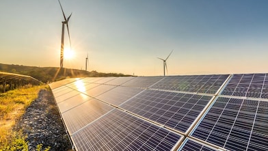 Solar panels and wind turbines generating renewable energy in a field at sunset.