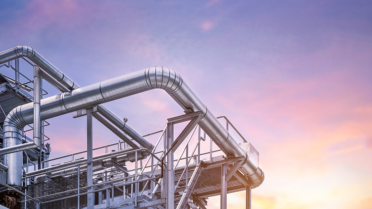 Industrial metal pipes and structures of a processing plant against a colorful sunset sky.