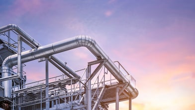 Industrial metal pipes and structures of a processing plant against a colorful sunset sky.