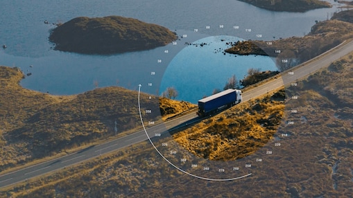 Aerial view of a truck travelling along a road through a coastal landscape, highlighted by a circular navigation graphic.
