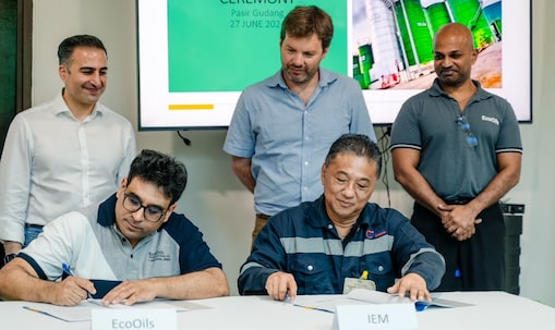 Rida from EcoOils signs a contract at a formal ceremony, seated at a table with colleagues standing behind him.