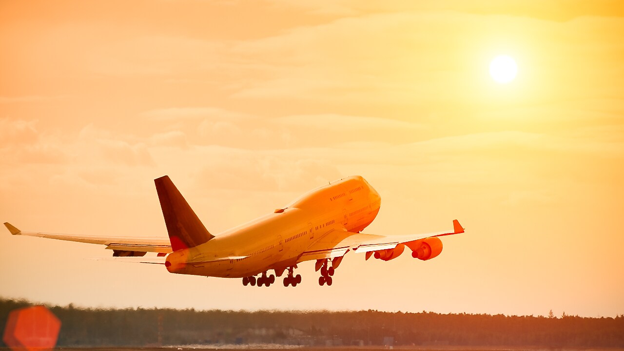 Commercial aeroplane lifting off the runway at sunset, with an orange glow reflecting off the fuselage and sky.