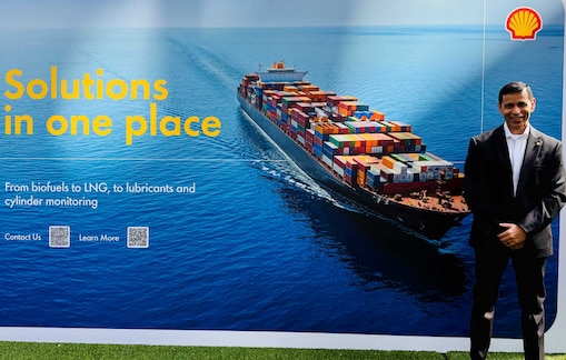 Rakshay Shah in a suit stands beside a Shell Marine display featuring a container ship at sea and the words “Solutions in one place.”