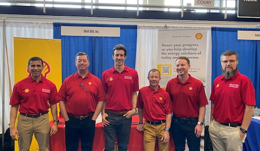 A group of six Shell representatives in red shirts pose together in front of an exhibition booth with Shell branding.