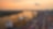 Aerial view of a busy container port with cranes and shipping containers, as a plane flies overhead during sunset with a city skyline in the background