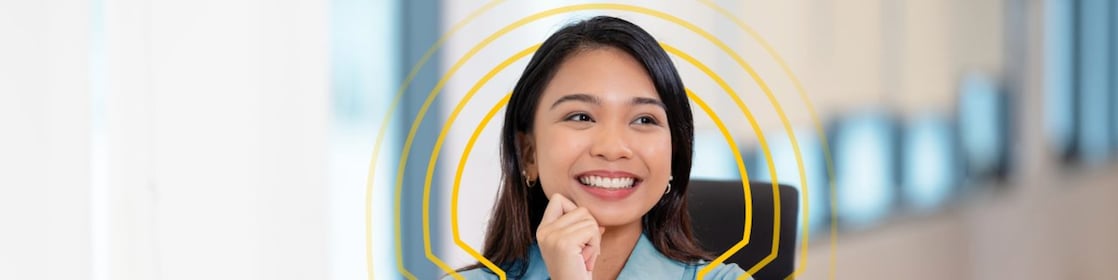 Person seated at a desk in a bright office, working on a laptop with a yellow drink placed nearby.