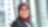 A young woman smiling, wearing a purple hijab, a dark jacket, and glasses, against office background.