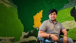 Person in a wheelchair wearing a Shell enABLE Network shirt, seated against a green and yellow moss wall.